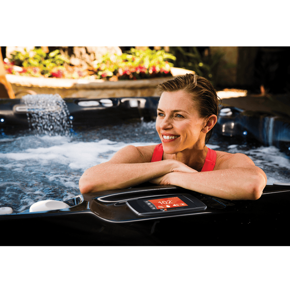 femme souriante dans le spa Caldera Niagara avec cascade Acquarella™ allumée et écran tactile visible