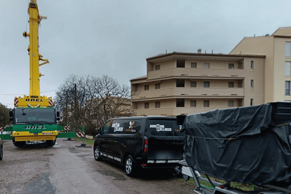Grue de manutention et camion Sommum Wellness sur un chantier, le spa sanglé sur sa remorque