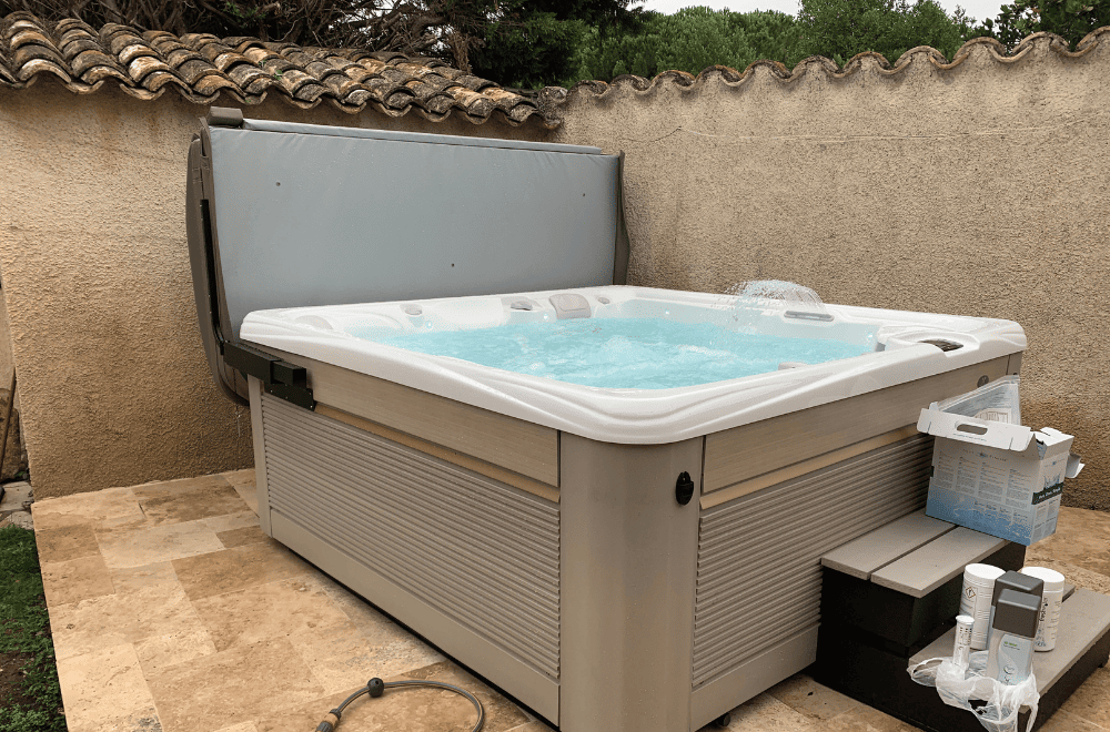 spa Caldera installé sur une terrasse carrelée, lève-couverture ouvert et marches d'accès